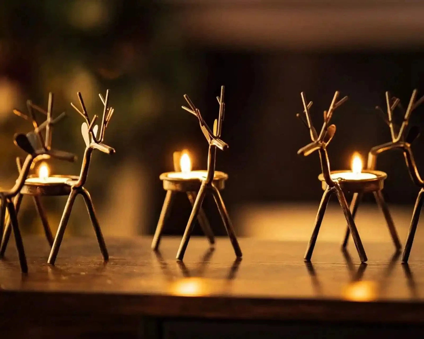 Small wooden reindeer figures with candle bases on a reflective surface.