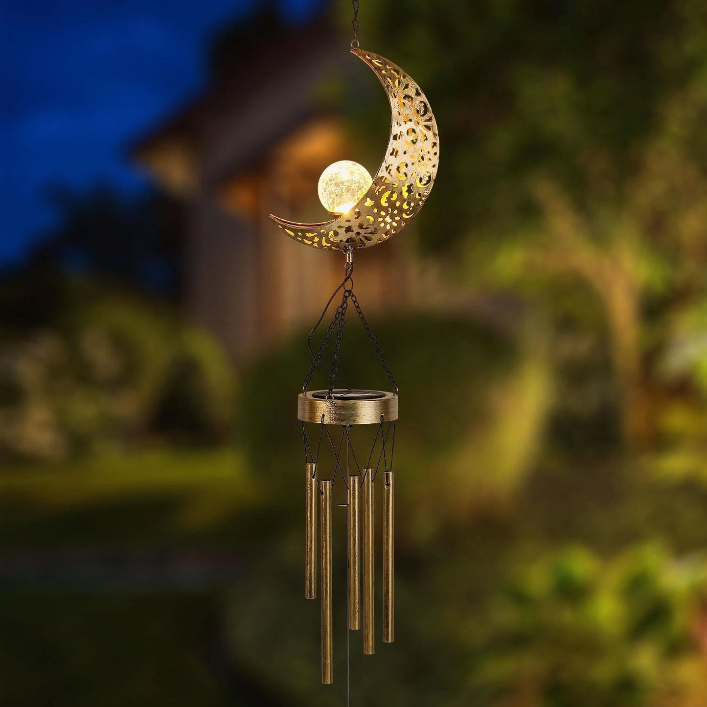 Decorative wind chime with moon design and lit bulb against a blurred garden background