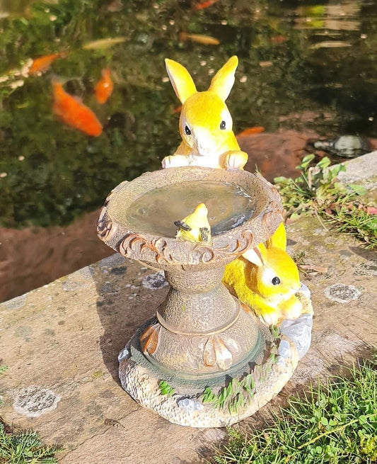 Decorative garden fountain with yellow frog figures near a pond with goldfish.