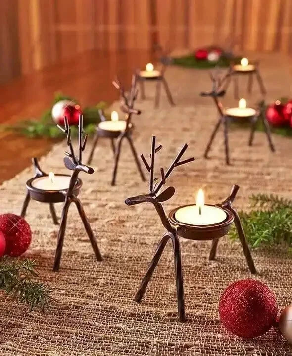 Decorative reindeer candle holders with candles on a textured surface with Christmas decorations.
