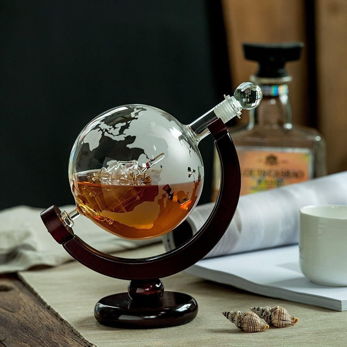 Globe-shaped decanter with liquid on a table with a bottle and cup in the background