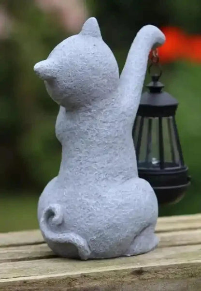 Stone cat figurine with one paw raised on a wooden surface outdoors