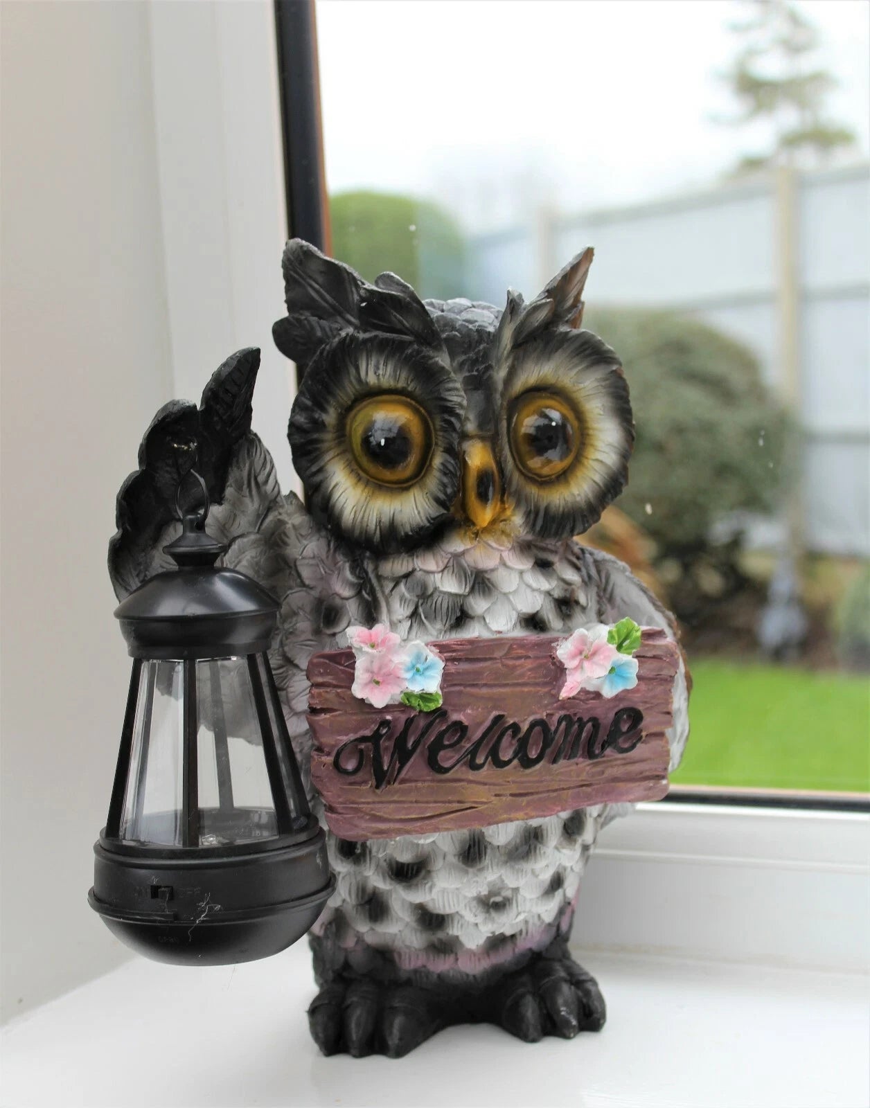 Decorative owl holding a 'Welcome' sign with a lantern, placed indoors near a window.