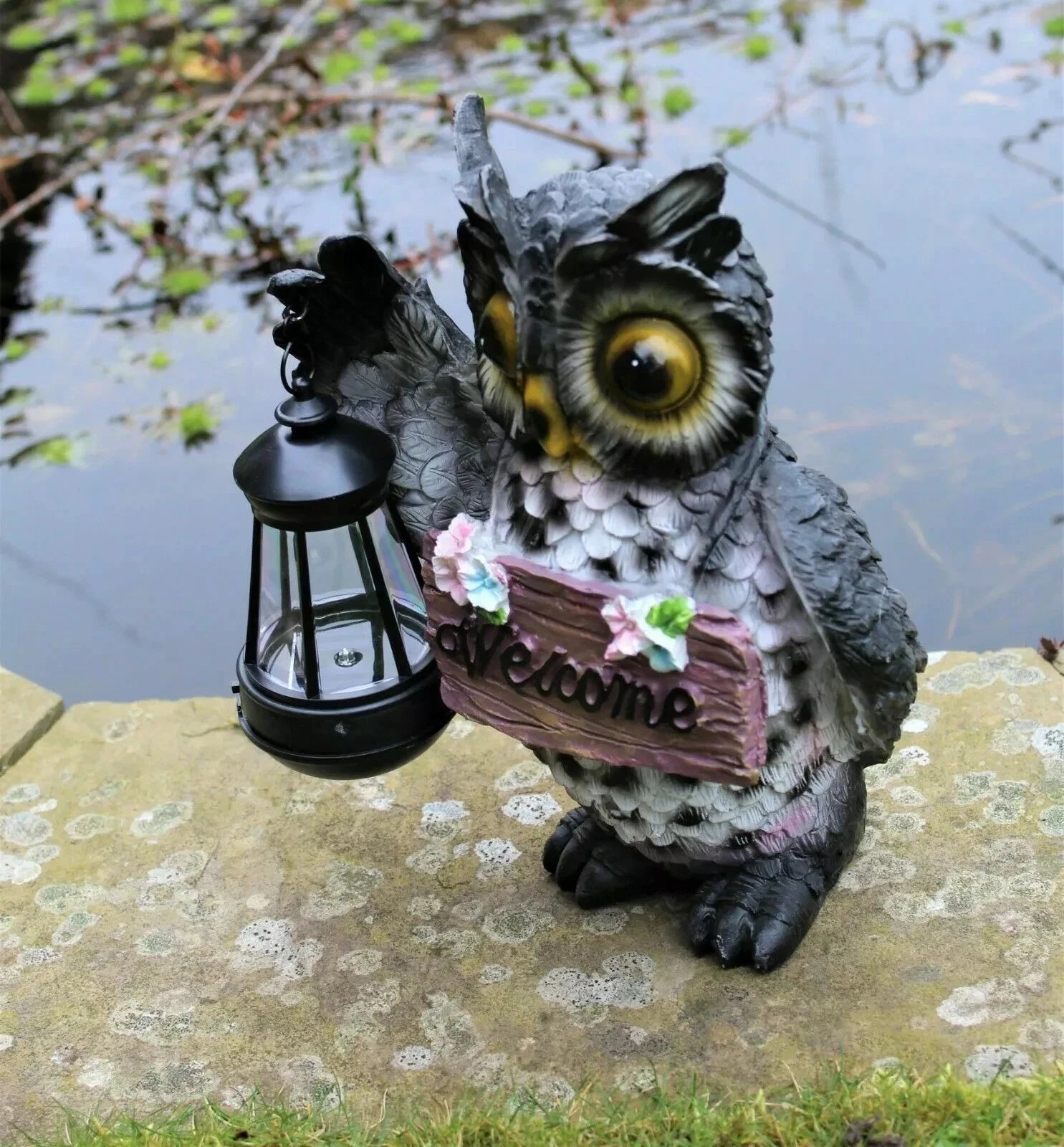 Owl decorative garden statue with lantern and 'welcome' sign on a stone ledge.