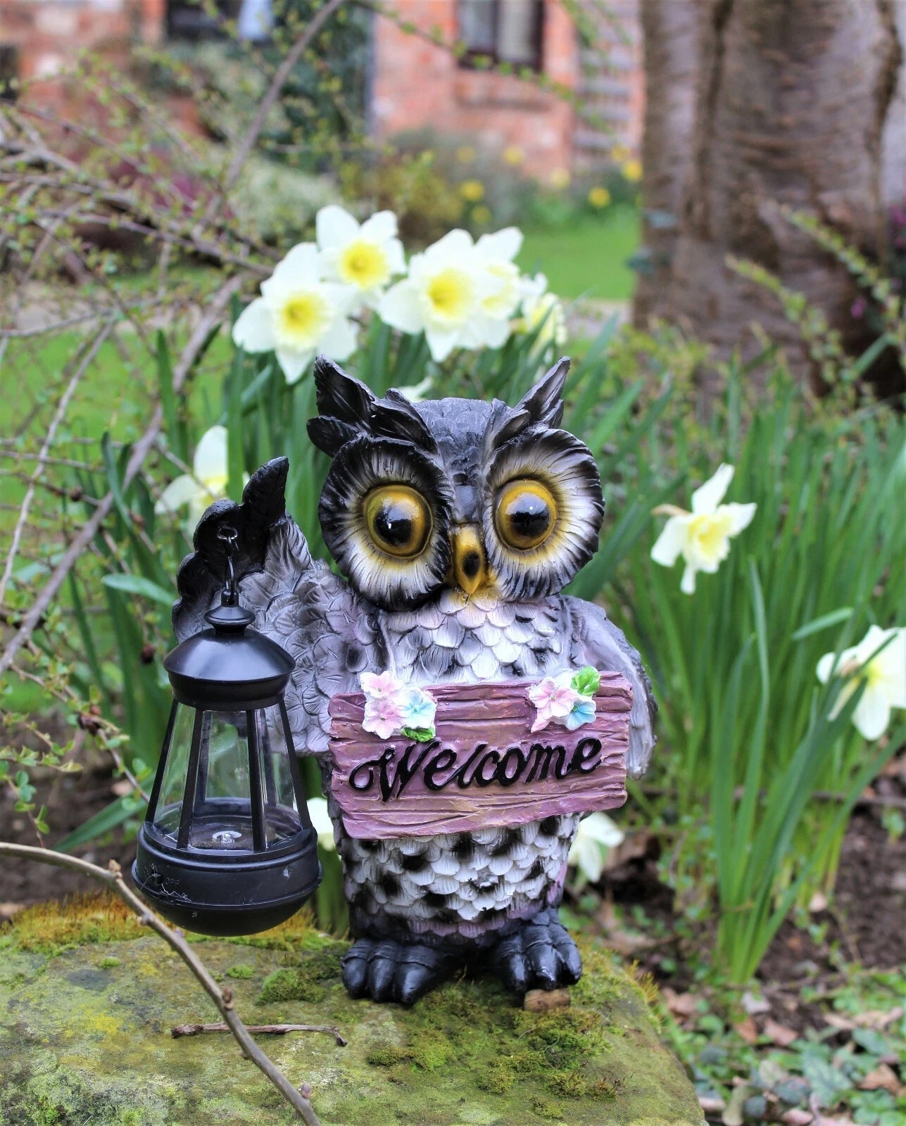 Decorative owl with a 'Welcome' sign and lantern in a garden setting