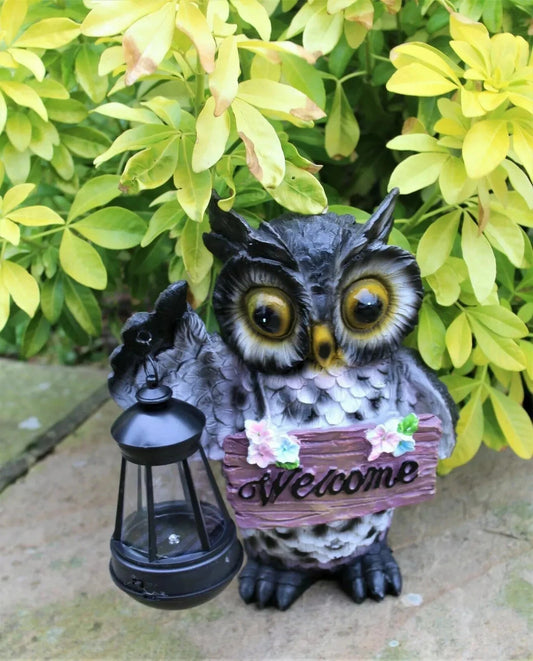 Owl figurine with a lantern and 'Welcome' sign in front of green foliage